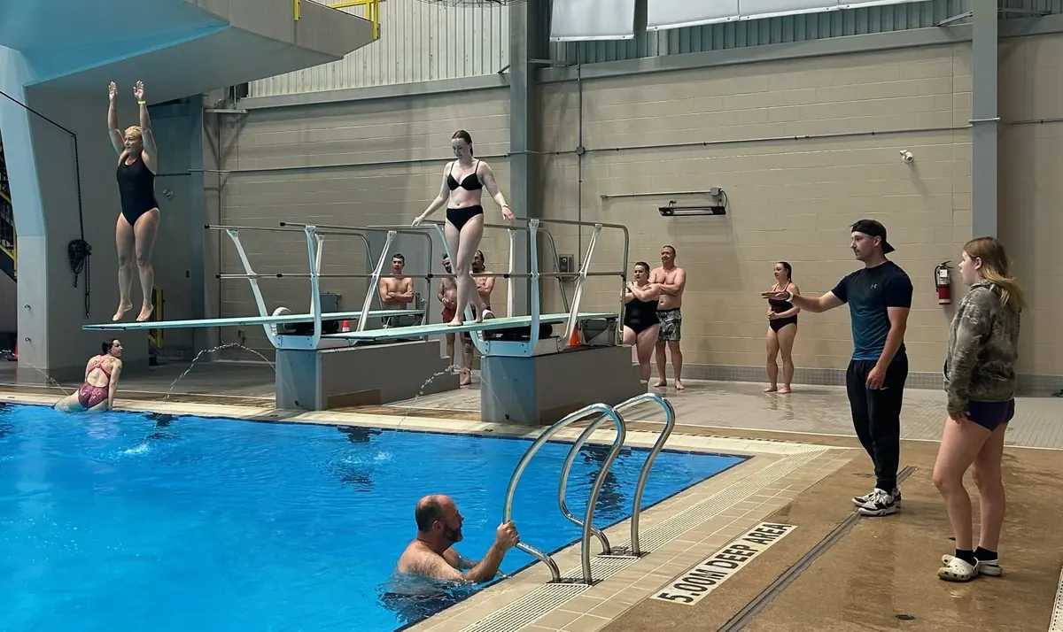 Two divers on the springboards at the Shaw Centre while other club members watch from the pool deck.